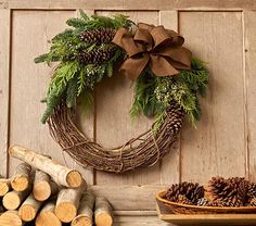 a wreath with pine cones and greenery is hung on the wall next to logs