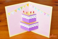 a birthday card with three candles on top of it, in front of a wooden table