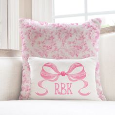 a pillow with a pink bow on it sitting on a white couch in front of a window