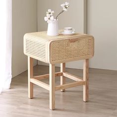 a wicker side table with two cups on it and flowers in a vase next to it