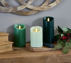 three candles sitting on top of a wooden table next to a cell phone and christmas greenery