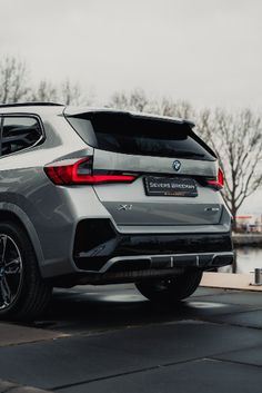 the rear end of a silver bmw suv parked in front of a body of water