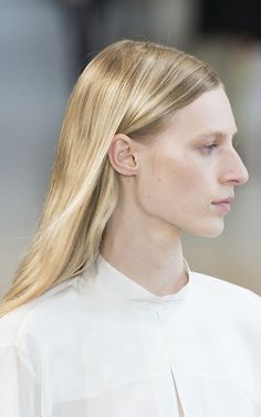 a woman with long blonde hair wearing a white shirt and looking off to the side