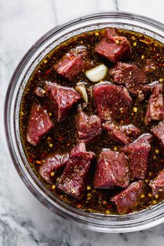 a glass bowl filled with meat and seasoning on top of a marble countertop