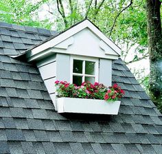 a window box with flowers in it on the roof of a house that is surrounded by trees