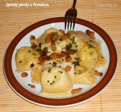 a white plate topped with ravioli covered in cheese and bacon next to a fork