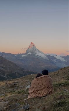 a person wrapped in a blanket sitting on top of a hill looking at the mountains