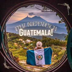 a man sitting on top of a bench holding a blue and white flag in front of a mountain