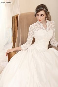 a woman sitting in a chair wearing a white wedding dress with long sleeves and lace detailing