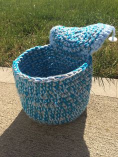 a crocheted basket sitting on top of a sidewalk next to a grass field