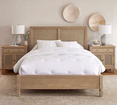 a bed with white sheets and pillows in a bedroom next to two wooden nightstands