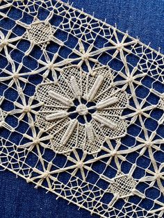 an intricately designed piece of cloth on a blue tablecloth with white crochet