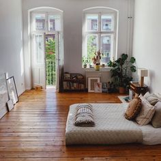 a bed sitting on top of a hard wood floor next to two windows in a living room