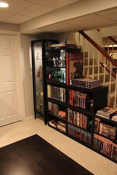 a living room filled with lots of dvd's next to a stair case full of movies