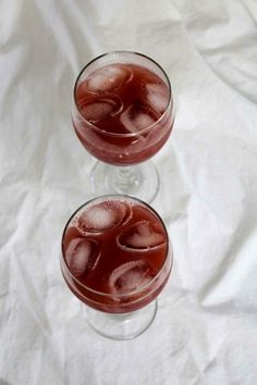 two glasses filled with drinks sitting on top of a white tablecloth covered floor next to each other