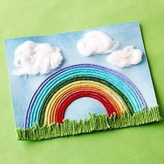 a paper cut out of grass with a rainbow in the sky and clouds above it