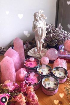 pink flowers and soaps on a table next to a statue in the shape of a cup