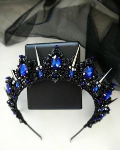 a tiara with blue and black jewels on it sitting next to a piece of cloth