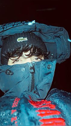 a man wearing a blue jacket and black hat covered in water droplets with his face partially hidden by the hood