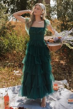 a woman in a green dress standing on a picnic blanket with her arms behind her head