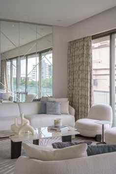 a living room filled with white furniture and large mirrors on the wall above it's windows