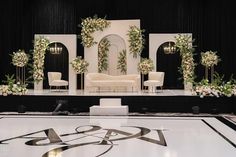 a stage set up for a wedding ceremony with white flowers and greenery on it