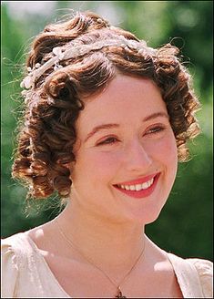 a woman with curly hair smiling at the camera and wearing a white dress on her head