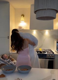 a woman holding a baby in her arms while standing next to a table with food on it