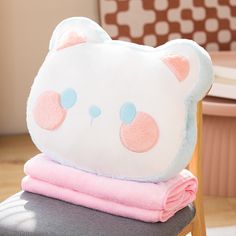 a teddy bear pillow sitting on top of a chair with pink and blue blankets around it