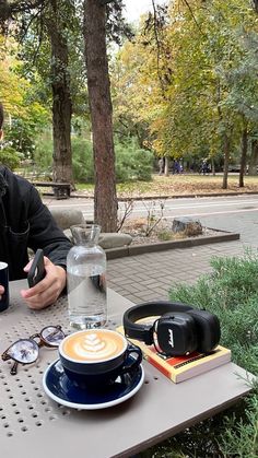 a man sitting at an outdoor table with coffee and other items on top of it