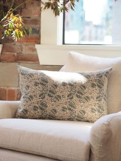 a white chair with a pillow on it in front of a brick wall and potted plant