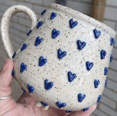 a hand holding a ceramic mug with blue hearts on it