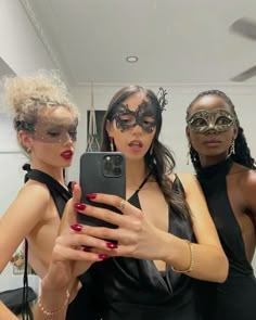 three women in black dresses are taking a selfie with a cell phone while wearing masks