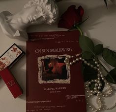 a red book sitting on top of a table next to a rose and some pearls