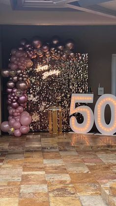 a 50th birthday party with balloons and lights on the wall, in front of a sign that reads 50