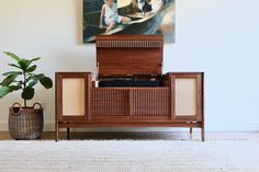 a painting hangs on the wall above a credenza with an antique record player