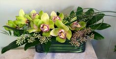 an arrangement of green orchids and greenery in a square vase