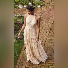 a woman in a long dress walking down a brick path with her hand on her hip