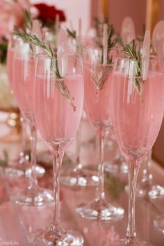 there are many wine glasses on the table with some flowers in them and one is filled with pink liquid