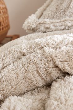 a close up of a bed with a white comforter on it and a wicker basket in the background