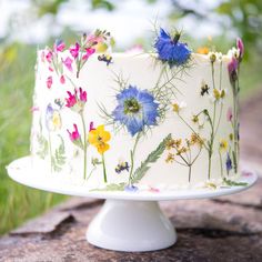 a white cake with flowers painted on it sitting on top of a stone slab in the grass