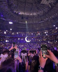 many people are taking pictures with their cell phones at an indoor concert venue while the moon is in the sky