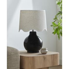 a black vase sitting on top of a wooden table next to a white and gray lamp