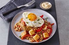 a plate topped with fried eggs, beans and vegetables next to a fork on a table