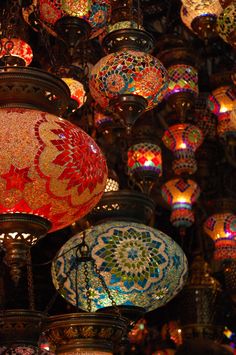 many colorful lights hanging from the ceiling in a room filled with other lamps and chandeliers