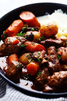 a pan filled with meat, potatoes and carrots on top of a white table cloth