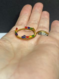 a person's hand holding two rings with different colored beads on them and one has a gold band