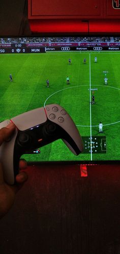 a person holding a video game controller in front of a tv screen with a soccer game on it