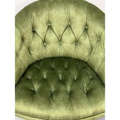 a green velvet chair with buttons on the back and arms, sitting in front of a white wall