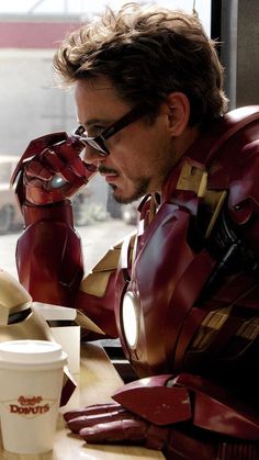 a man dressed as iron man sitting at a table with a cup of coffee in front of him